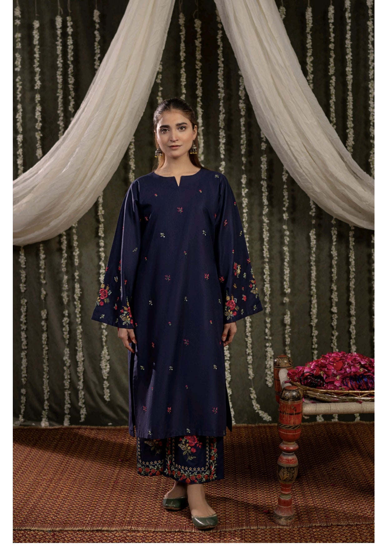 Woman wearing a navy blue embroidered outfit standing in front of decorative curtains.