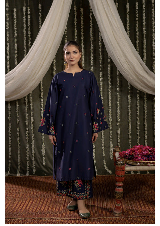 Woman wearing a navy blue embroidered outfit standing in front of decorative curtains.