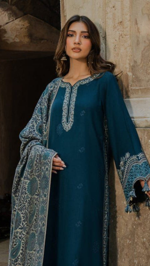 Woman in a teal traditional outfit with embroidery standing in front of a stone wall.