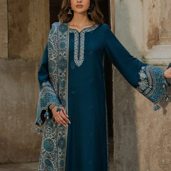 Woman in a long, dark blue embroidered dress standing in front of stone architecture.