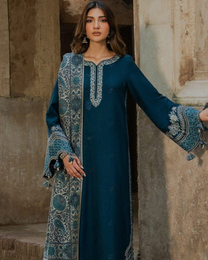 Woman in a long, dark blue embroidered dress standing in front of stone architecture.